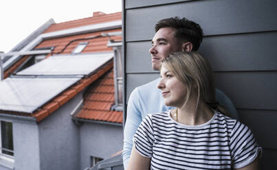 Nachdenkliches junges Paar lehnt auf dem Balkon an der Wand - UUF28832