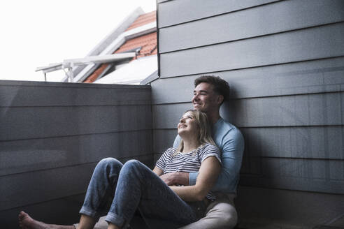 Happy young couple sitting on balcony - UUF28834