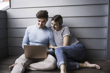 Lächelndes junges Paar benutzt gemeinsam einen Laptop - UUF28840