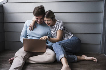 Glückliches junges Paar benutzt gemeinsam einen Laptop - UUF28841