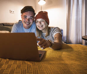 Happy young couple using laptop together at home - UUF28860