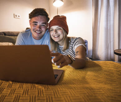 Glückliches junges Paar, das gemeinsam zu Hause einen Laptop benutzt - UUF28860