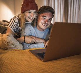 Glückliche Frau und Mann mit Laptop auf dem Sofa zu Hause - UUF28863
