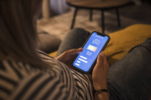 Young woman operating electric car charging mobile app at home - UUF28870