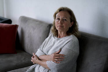 Senior woman sitting with arms crossed on sofa at home - ANNF00282