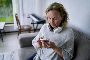 Senior woman using smart phone on sofa at home - ANNF00291