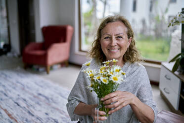 Glückliche ältere Frau mit einer Vase voller Blumen zu Hause - ANNF00295