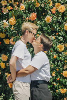 Lesbisches Paar, das sich vor einer Mauer mit Rosen küsst - VSNF01061