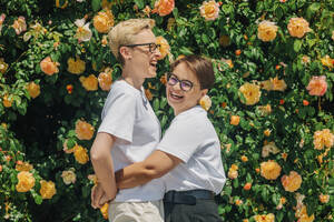 Glückliches lesbisches Paar vor einer Mauer mit Rosen - VSNF01062