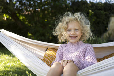 Lächelndes Mädchen sitzt auf Hängematte im Garten - SVKF01432