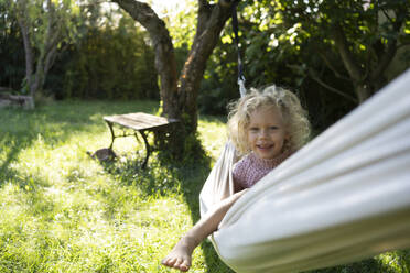 Happy girl sitting on hammock in garden - SVKF01434