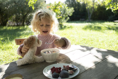 Happy girl feeding food to stuffed toy in garden - SVKF01437