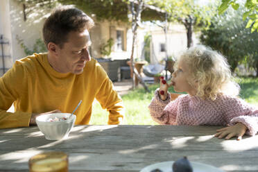 Vater sieht seine Tochter an, die im Garten Beeren isst - SVKF01439