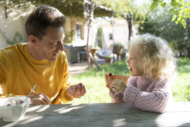 Vater und Tochter essen Obst aus einer Schale im Garten - SVKF01440