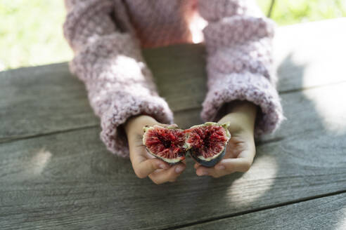 Hands of girl holding fig on table - SVKF01441