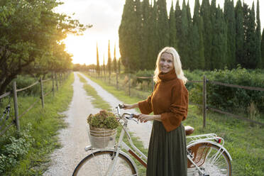 Smiling woman standing next to bicycle on footpath - SVKF01447