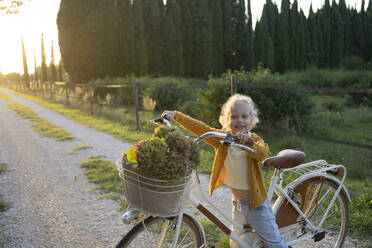 Smiling girl holding bicycle handle on footpath - SVKF01451