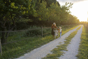 Mutter und Tochter gehen mit dem Fahrrad auf dem Fußweg bei Sonnenuntergang - SVKF01455