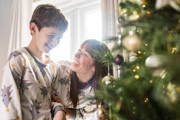 Glückliche Mutter mit Sohn vor dem Weihnachtsbaum zu Hause stehend - WPEF07412