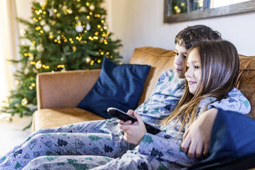 Lächelndes Mädchen, das mit seinem Bruder zu Hause zur Weihnachtszeit fernsieht - WPEF07415