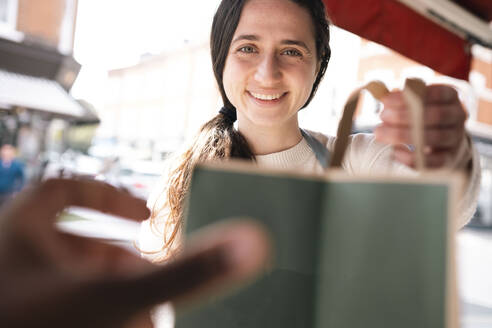 Grocer giving shopping bag to customer at store - AMWF01386