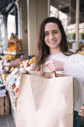Happy grocer standing with paper bag at vegetable stall - AMWF01401
