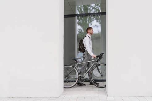 Businessman wheeling with bicycle in office corridor - OSF01657