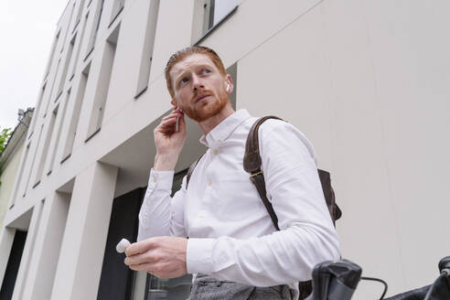 Thoughtful businessman wearing wireless in-ear headphones at office - OSF01665