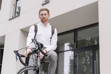 Geschäftsmann sitzt auf dem Fahrrad vor dem Büro - OSF01668