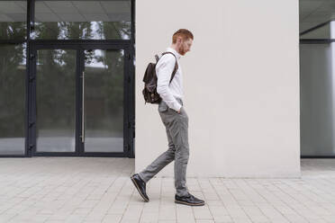 Businessman with backpack walking outside office - OSF01670
