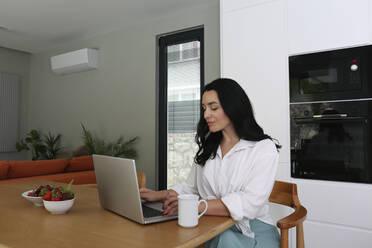 Frau mit Laptop am Tisch sitzend zu Hause - SYEF00455