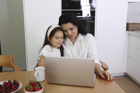 Lächelnde Frau und Tochter führen einen Videoanruf über einen Laptop zu Hause - SYEF00459