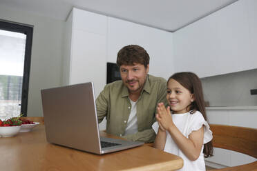 Lächelnde Tochter mit verschränkten Händen vor dem Laptop des Vaters zu Hause - SYEF00464