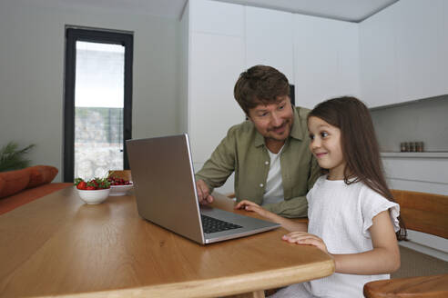 Lächelndes Mädchen lernt mit seinem Vater zu Hause den Umgang mit dem Laptop - SYEF00466