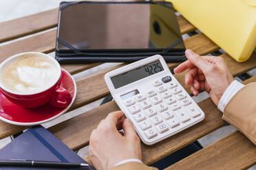 Hand einer Geschäftsfrau mit Taschenrechner und Kaffee auf dem Tisch - MGRF01015