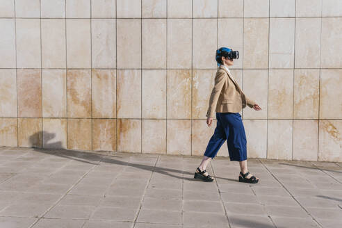 Geschäftsfrau mit Virtual-Reality-Headset läuft vor einer Wand - MGRF01019