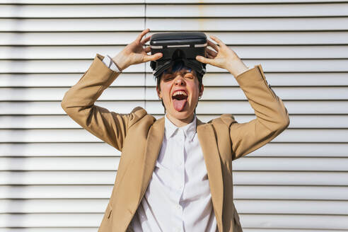 Businesswoman sticking out tongue wearing wearing virtual reality headset - MGRF01022