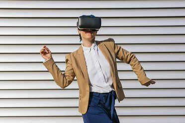 Sorglose Geschäftsfrau mit Virtual-Reality-Headset tanzt vor einer Wand - MGRF01027