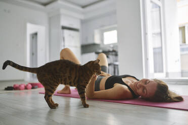 Happy young woman stroking cat and exercising at home - ANNF00313