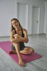 Smiling young woman sitting on mat at home - ANNF00314