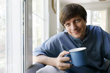 Lächelnder Mann trinkt Tee im Wohnzimmer - TYF00795