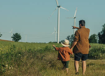 Vater und Sohn gestikulieren in Richtung Windkraftanlagen auf einem Feld - VSNF01080