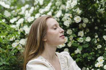 Young woman with eyes closed by white flower bush - SEAF01965