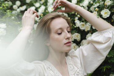 Young woman with arms raised by white flower bush - SEAF01966