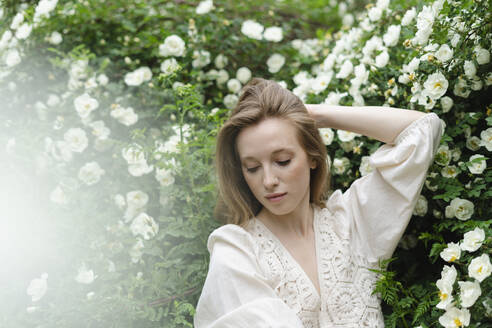 Junge Frau mit Hand im Haar an weißem Blumenbusch - SEAF01967