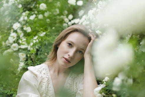 Junge schöne Frau mit Hand im Haar an weißem Blumenbusch - SEAF01968