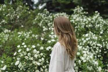 Woman with long blond hair standing by white flower bush - SEAF01973