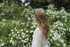 Frau mit langen blonden Haaren an einem weißen Blumenbusch stehend - SEAF01973