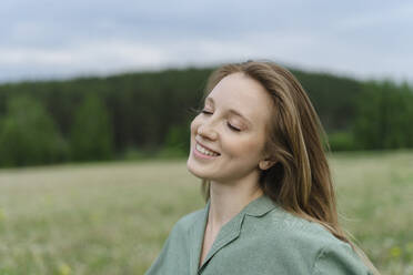 Lächelnde junge Frau mit geschlossenen Augen auf einem Feld - SEAF01985