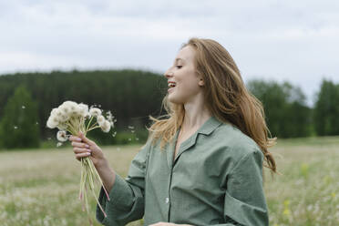 Lächelnde junge Frau hält Löwenzahn auf einem Feld - SEAF01990
